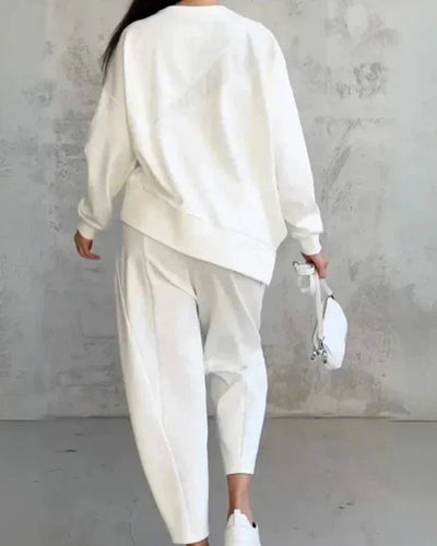 Femme en tenue décontractée blanche, portant un sweat et un pantalon ample, tenant un petit sac blanc. Style minimaliste et moderne.