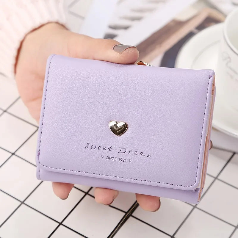 Portefeuille violet en cuir avec un motif de cœur argenté, posé sur une table à carreaux. Accessoire mode élégant pour femmes, tendance et pratique.
