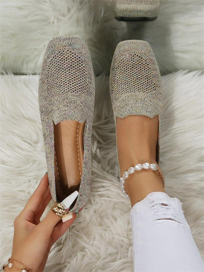 Chaussures plates en tricot beige sur tapis blanc, portées avec un jean blanc déchiré et un bracelet de perles. Mode féminine élégante et décontractée.