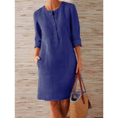 Robe en lin bleu avec manches longues retroussées, boutons sur le devant, poches, portée par une femme tenant un sac en osier. Mode décontractée élégante.