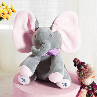 Peluche éléphant gris avec oreilles roses, nœud papillon violet à pois, sur table rose. Jouet interactif pour enfants, décor chambre bébé.
