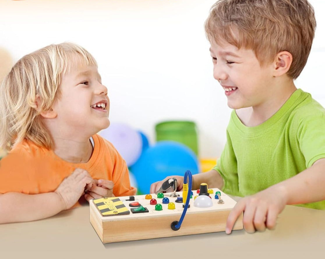 Deux enfants jouent avec un tableau sensoriel en bois, comprenant boutons colorés et éléments interactifs, favorisant l'apprentissage et la motricité.