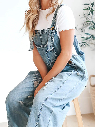 Femme en salopette en jean décontractée, assise sur un tabouret, portant un t-shirt blanc. Mode tendance, style décontracté, vêtements en denim.