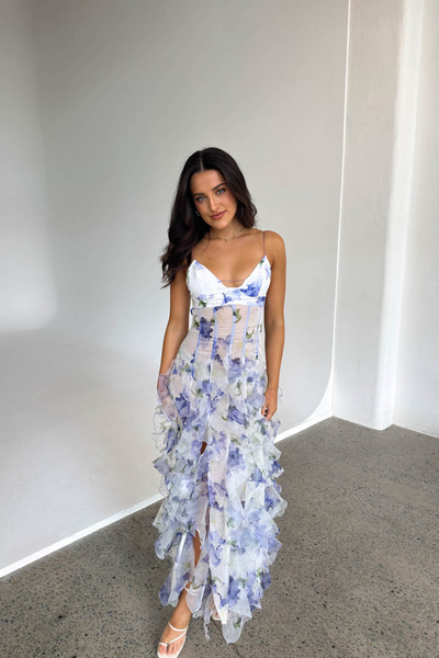 Jeune femme portant une robe longue à motifs floraux bleus et blancs, posant dans un intérieur moderne. Mode élégante, tenue estivale chic.