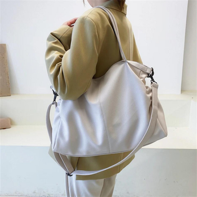 Femme portant un grand sac à main en cuir blanc cassé, élégant et moderne, avec une bandoulière ajustable, idéal pour la mode urbaine.