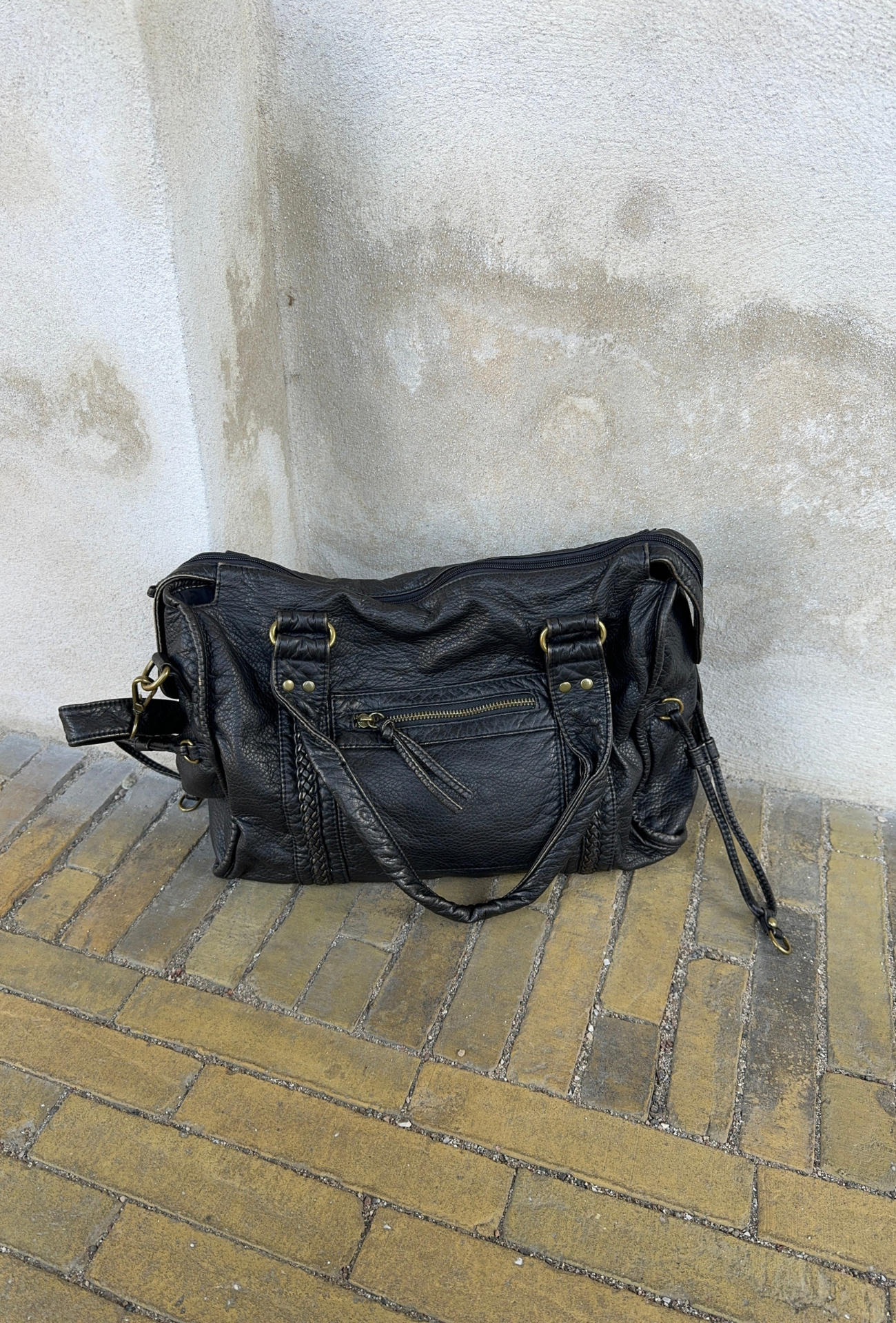 Sac à main en cuir noir sur sol en briques jaunes, avec fermetures éclair dorées et anses robustes. Accessoire mode élégant et tendance.
