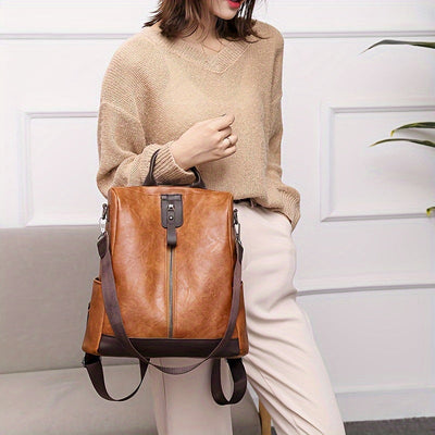 Femme portant un sac à dos en cuir marron élégant, design moderne, avec fermeture éclair centrale, tenue décontractée beige, intérieur chic.