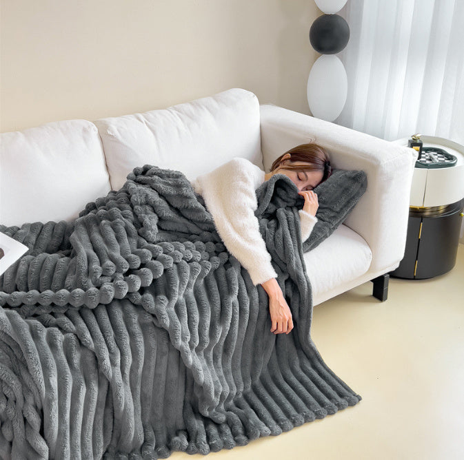 Femme endormie sur canapé blanc, enveloppée dans une couverture en fausse fourrure grise. Décor moderne, ambiance cosy et relaxante.