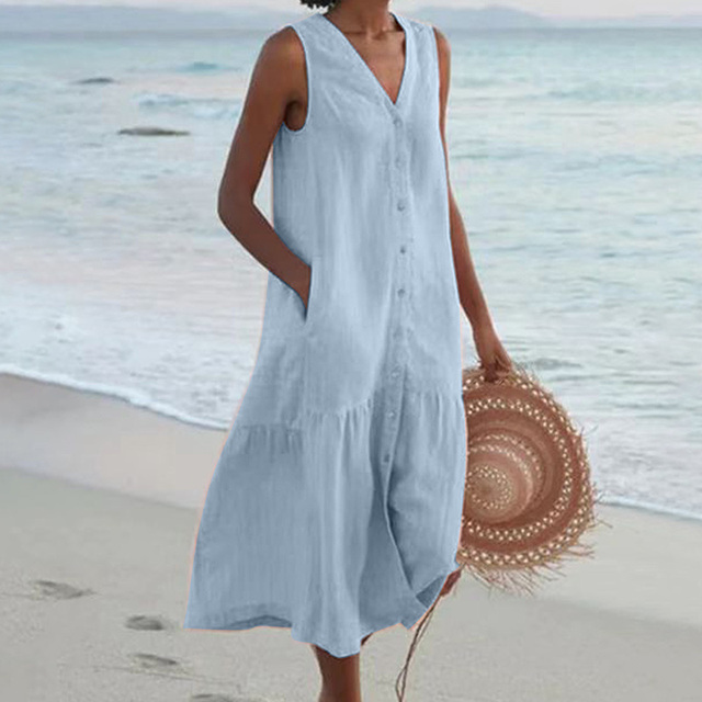 Robe d'été bleue sans manches sur une femme tenant un chapeau de paille, plage en arrière-plan. Mode plage, tenue estivale élégante.