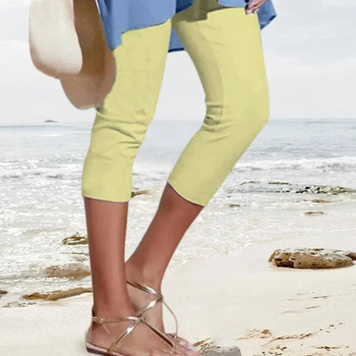 Personne en pantacourt jaune et sandales dorées marchant sur une plage, tenant un chapeau de paille. Mode estivale, bord de mer, tenue décontractée.