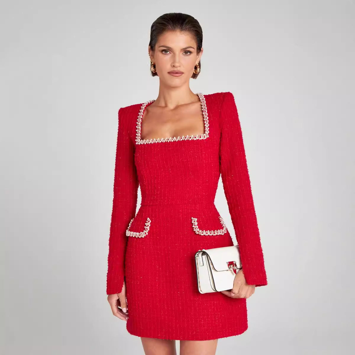 Femme portant une robe rouge élégante avec détails perlés, manches longues et col carré, tenant un sac à main argenté. Mode chic et tendance.