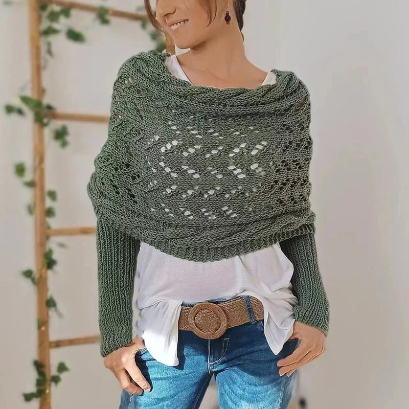 Femme portant un châle tricoté vert sur un pull blanc, jeans et ceinture marron. Échelle en bois et plantes en arrière-plan. Mode automne-hiver.