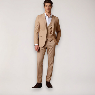 Homme en costume beige élégant, chemise blanche, cravate absente, chaussures marron, pose debout. Mode masculine, tenue formelle chic.