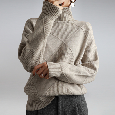 Femme portant un pull en laine beige à col roulé, motif géométrique, manches longues, style automne-hiver, mode élégante et confortable.