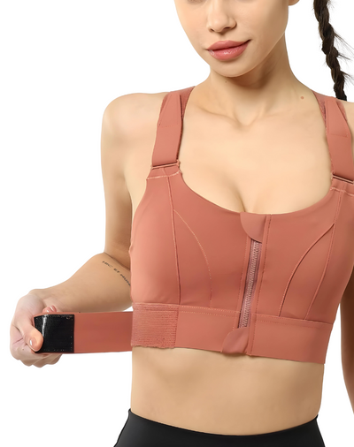 Femme portant une brassière de sport rose avec fermeture éclair, ajustant la sangle. Vêtement de sport confortable et tendance pour fitness.
