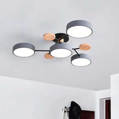 Plafonnier moderne à LED avec quatre abat-jours circulaires gris et détails en bois, monté au plafond blanc d'un salon contemporain.