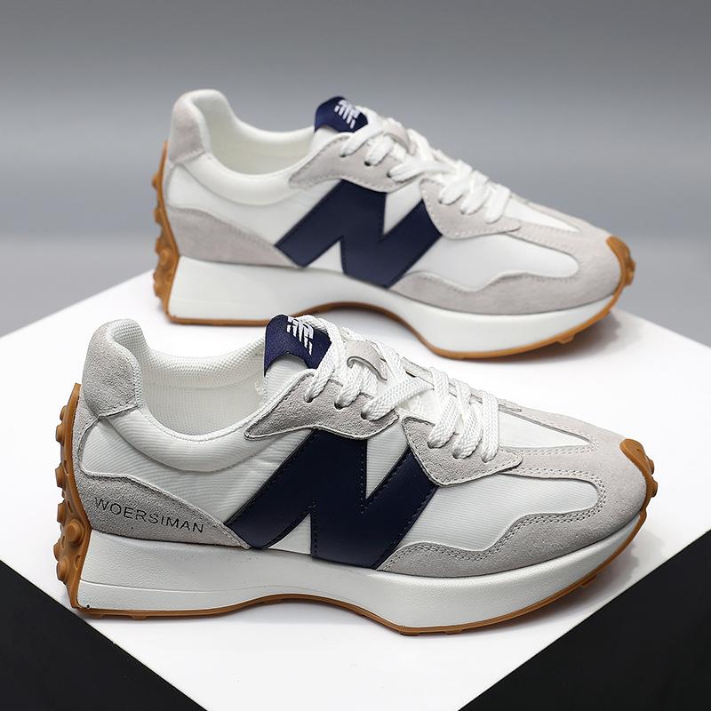 Chaussures de sport blanches et grises avec semelle en caoutchouc marron, logo bleu foncé, style moderne, posées sur fond gris.