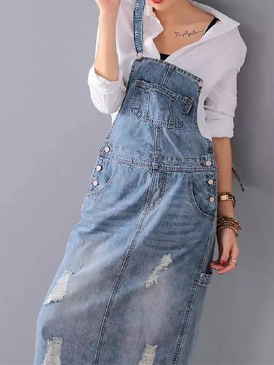 Femme portant une robe salopette en jean délavé avec chemise blanche, style décontracté, mode féminine tendance, look moderne et chic.