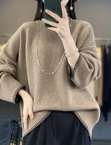 Femme portant un pull en laine beige ample, collier perles, tenant un smartphone. Mode automne-hiver, style décontracté chic, tendance féminine.