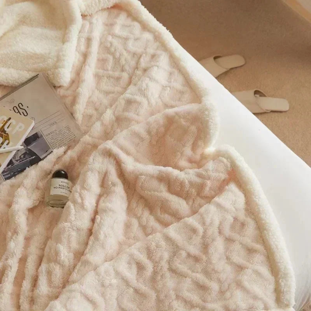 Couverture en fausse fourrure beige sur un lit, avec magazine et flacon de parfum. Décor cocooning, ambiance chaleureuse et élégante.