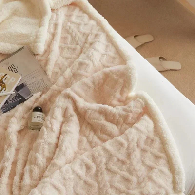 Couverture en fausse fourrure beige sur un lit, avec magazine et flacon de parfum. Décor cocooning, ambiance chaleureuse et élégante.