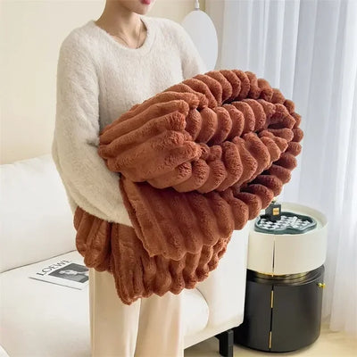Personne tenant une couverture en peluche marron, douce et texturée, dans un salon moderne. Décor intérieur chaleureux, rideaux blancs en arrière-plan.