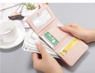 Portefeuille rose ouvert avec billets de banque et cartes de crédit, tenu par des mains féminines, tasse de café et magazine en arrière-plan.