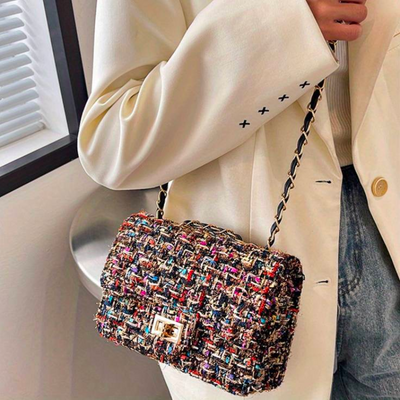 Sac à main en tweed multicolore avec chaîne dorée, porté par une personne en veste blanche. Accessoire mode élégant et tendance.