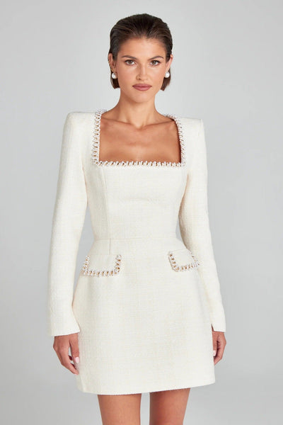Robe blanche élégante à manches longues, col carré, ornée de détails perlés, portée par une femme. Mode féminine chic et sophistiquée.
