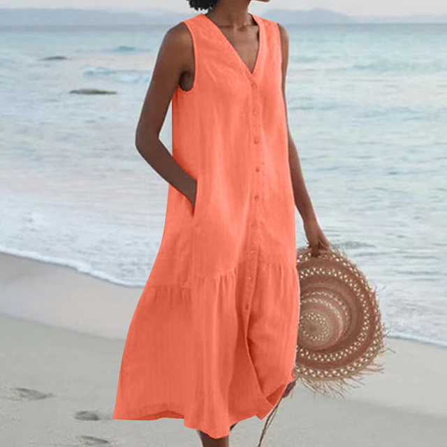 Robe d'été orange sans manches sur une femme à la plage, tenant un chapeau de paille. Mode estivale, tenue décontractée, bord de mer.