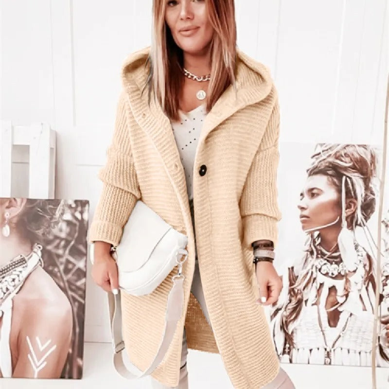 Femme portant un manteau en laine beige avec capuche, sac blanc à l'épaule, posant devant des portraits artistiques. Mode automne-hiver chic.