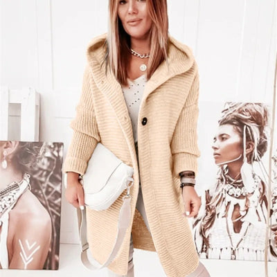 Femme portant un manteau en laine beige avec capuche, sac blanc à l'épaule, posant devant des portraits artistiques. Mode automne-hiver chic.