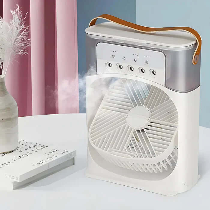 Ventilateur portable blanc avec poignée en cuir, fonction brumisateur, posé sur une table près d'un vase et de livres, rideaux roses en arrière-plan.