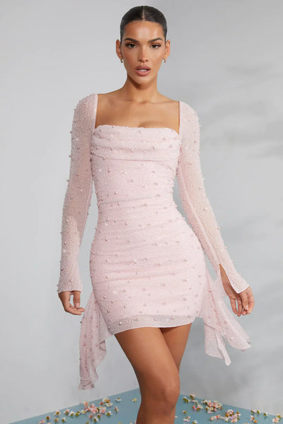 Robe rose pâle ajustée à manches longues, ornée de perles, portée par une femme. Mode élégante, tenue de soirée chic, style moderne.