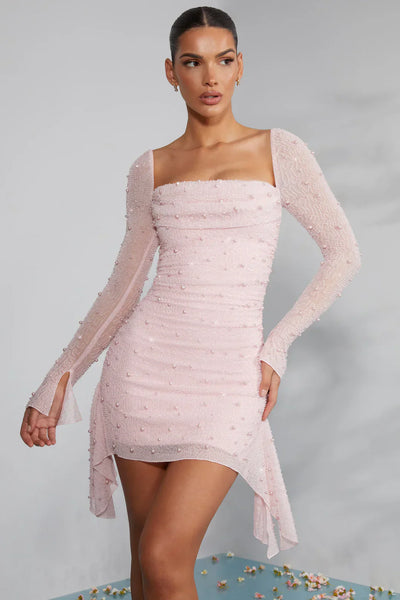 Robe rose pâle à manches longues, ornée de perles, portée par une femme. Style élégant et moderne, idéal pour soirées et événements spéciaux.
