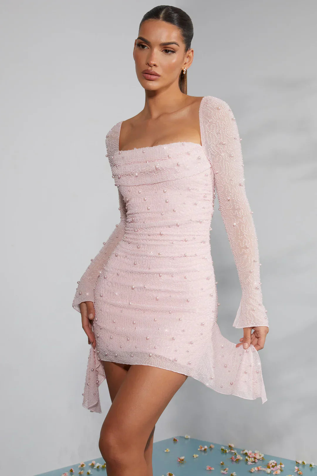 Robe rose pâle à manches longues, ornée de perles, portée par une femme. Style élégant et moderne, idéal pour soirées et événements spéciaux.
