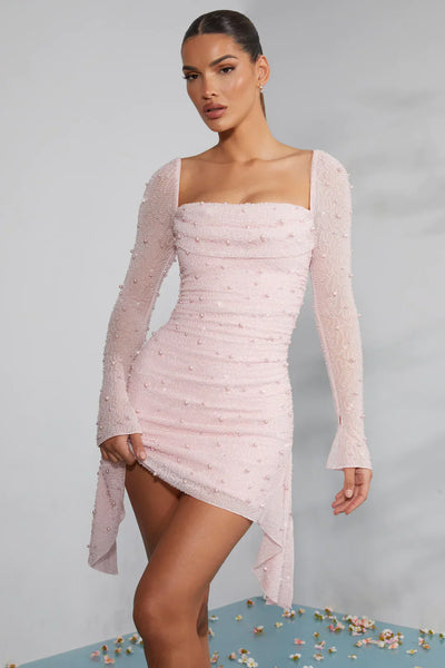 Robe rose pâle à manches longues, ornée de perles, avec ourlet asymétrique. Mode élégante, tenue de soirée chic, style moderne.