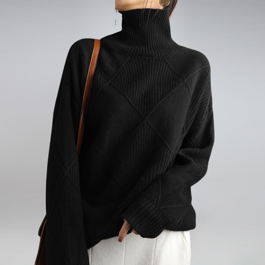 Femme portant un pull noir à col roulé en maille texturée, avec un sac à bandoulière marron, sur fond gris. Mode automne-hiver élégante.