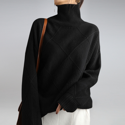 Femme portant un pull noir à col roulé en maille texturée, avec un sac à bandoulière marron, sur fond gris. Mode automne-hiver élégante.