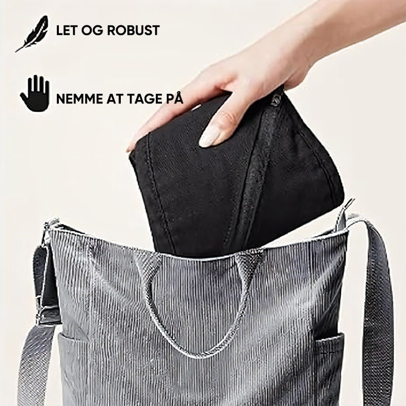 Sac à main gris avec une main insérant une pochette noire. Texte en danois: "Let og robust, nemme at tage på". Accessoire mode pratique et élégant.