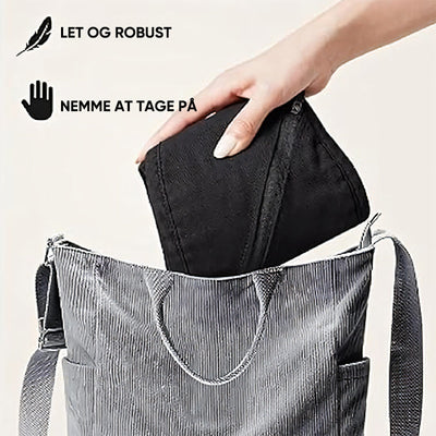 Sac à main gris avec une main insérant une pochette noire. Texte en danois: "Let og robust, nemme at tage på". Accessoire mode pratique et élégant.