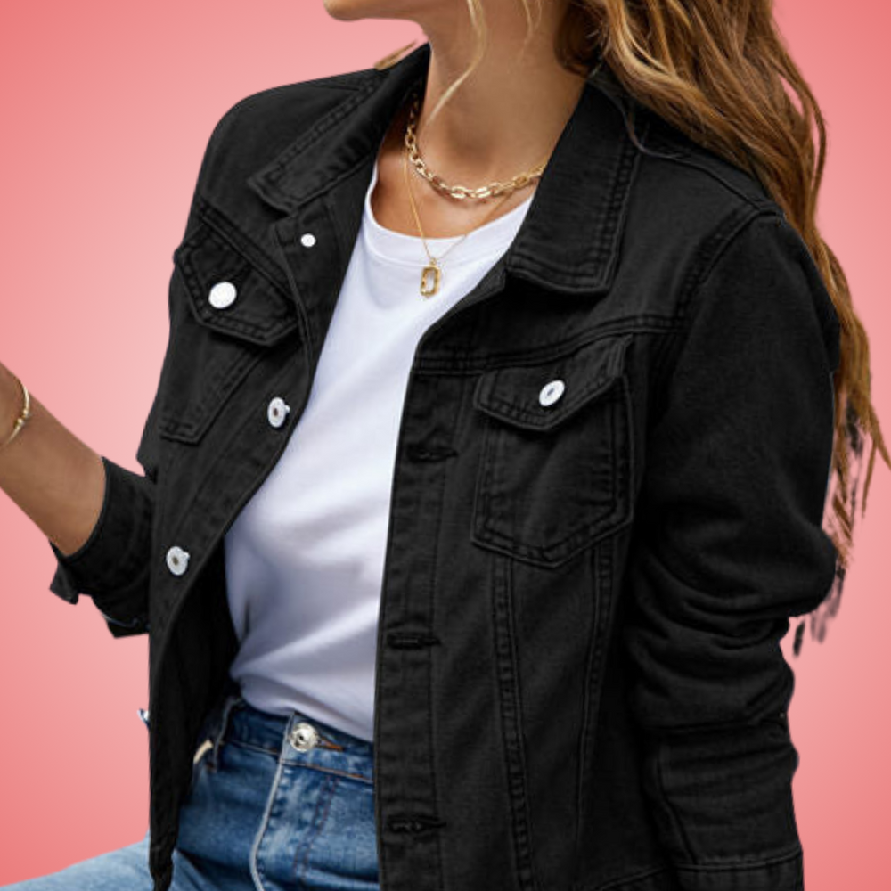 Veste en jean noire pour femme, portée sur un t-shirt blanc, avec un collier doré, fond rose. Mode féminine, style décontracté, tendance actuelle.
