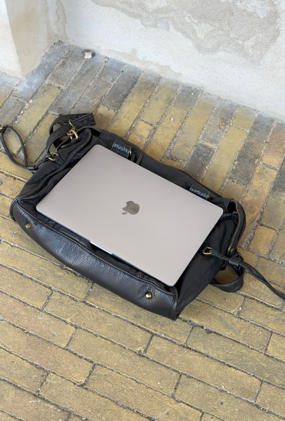 Ordinateur portable Apple MacBook argenté dans un sac en cuir noir sur un sol en briques jaunes. Technologie, mobilité, travail nomade.