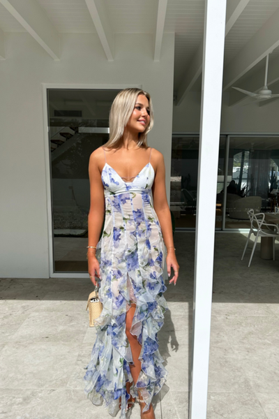 Femme en robe longue à fleurs bleues et blanches, posant sur une terrasse moderne. Style estival, élégance, mode féminine, extérieur lumineux.