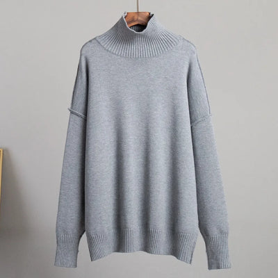 Pull-over gris à col roulé en laine, manches longues, style décontracté, suspendu sur un cintre en bois, fond gris clair. Mode hiver, vêtement chaud.