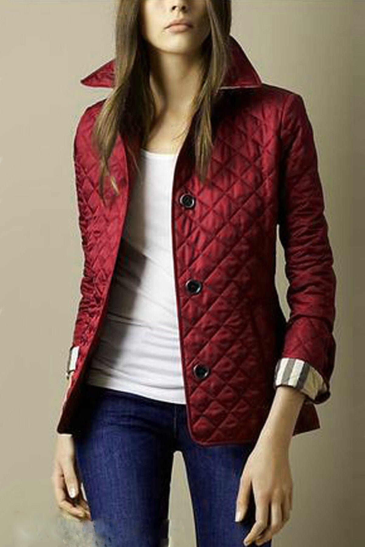 Femme portant une veste matelassée rouge avec boutons noirs, chemise blanche et jean bleu. Mode automne, style élégant et décontracté.