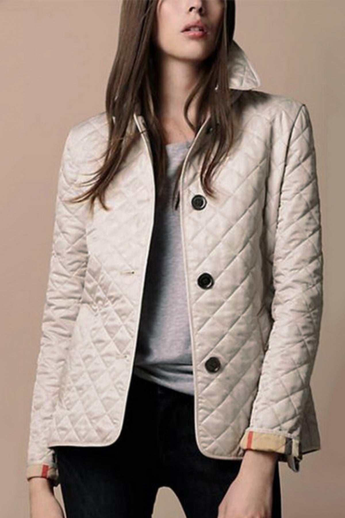 Femme portant une veste matelassée beige élégante, boutons noirs, col relevé, sur un fond neutre. Mode automne, style chic et moderne.