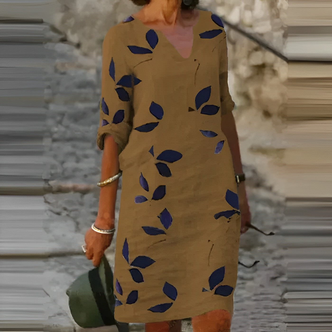 Robe marron à manches longues avec motifs de feuilles bleues, femme tenant un chapeau vert, style décontracté, mode automne, rue pavée.