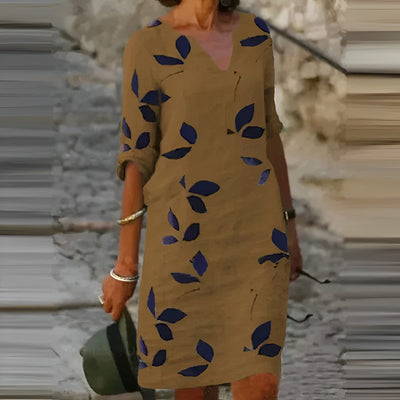Robe marron à manches longues avec motifs de feuilles bleues, femme tenant un chapeau vert, style décontracté, mode automne, rue pavée.