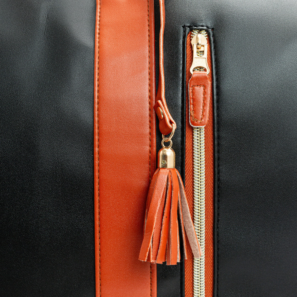 Gros plan d'un sac à main en cuir noir avec fermeture éclair dorée, bande et pompon en cuir marron. Accessoire de mode élégant et tendance.